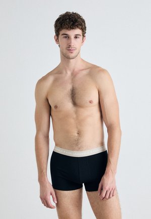 Sorte boxer briefs med en grå talje, der har teksten "KARL LAGERFELD". Stoffet ser glat og strækbart ud. Modellen står med selvtillid.