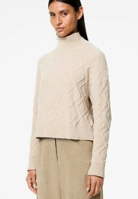 Maglione beige a collo alto in maglia con un motivo a rombi testurizzato, design cropped e orli a coste sulle maniche e sul fondo.