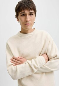 Cremefarvet strikket sweater med ribbestrikket halsudskæring og manchetter. Har en afslappet pasform, blød tekstur og lange ærmer.