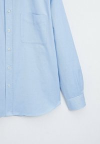 Chemise bleu clair à manches longues avec poche poitrine, poignets boutonnés et ourlet incurvé sur fond blanc.