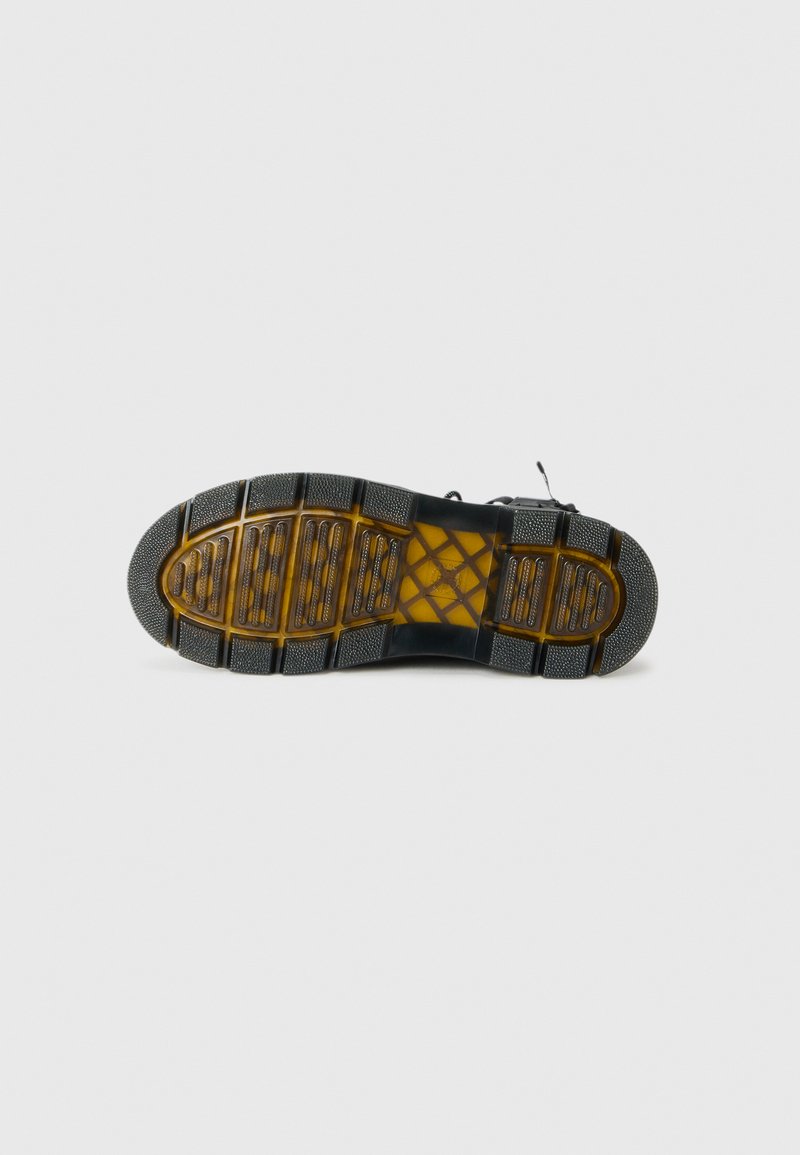 Semelle d'une botte noire avec une semelle translucide marron, montrant un grip texturé détaillé et un design de semelle segmenté sur fond uni.
