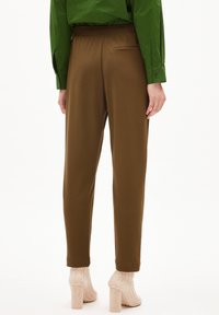 Brązowe tapered pants wykonane z gładkiego materiału, z elastycznym pasem i tylną kieszenią. Noszone z beżowymi, prążkowanymi szpilkami.