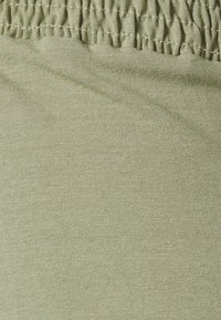 Tecido verde oliva claro com uma textura suave e cintura elástica franzida. Um brilho subtil acrescenta profundidade ao material.