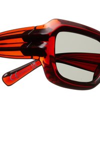 Lunettes de soleil en acétate rouge avec un design audacieux, une forme surdimensionnée et des verres sombres. Accentées de rayures noires sur les branches.