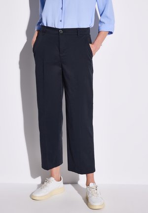 Pantaloni cropped blu navy realizzati in tessuto leggero, con chiusura a pulsante, tasche laterali e taglio dritto. Indossati con sneakers bianche.