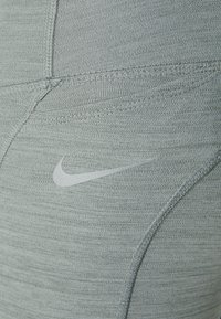 Leggings de sport gris clair en tissu texturé, avec un logo Nike subtil en argent et des coutures à plat pour un confort accru.
