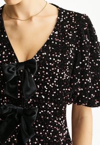 Black sequined dress featuring puff sleeves, velvet bows at the front, and a deep V-neckline with a shimmering texture throughout.