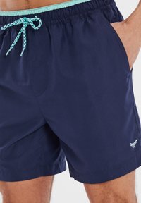 Bañador azul marino de tela ligera, con una suave cintura elástica, cordón de color verde menta y bolsillos laterales.