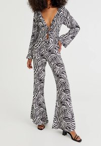 Zebra-print jumpsuit met een diepe V-hals, gefronste randen, lange mouwen en uitlopende benen. Gemaakt van lichte stof, met zwart-witte patronen.