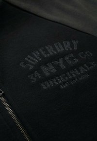 Zwarte zip-up hoodie van een katoenmix, met getextureerde zwarte borduursels met merknaam en ontwerpdetails, zilveren rits en gladde stofafwerking.