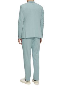 Lichtblauw pak van gladde stof, met een enkelrijig ontwerp, broek met rechte pijpen en witte sneakers. Geen zichtbare patronen.