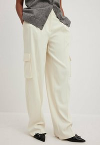 Crème-kleurige wijde cargo-broek met patchzakken. De stof heeft een gladde textuur. Gecombineerd met zwarte puntige schoenen.