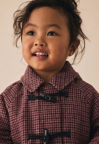 Manteau à carreaux roses avec un col montant et des fermetures à bascule noires. Présente un tissu texturé et une coupe décontractée.