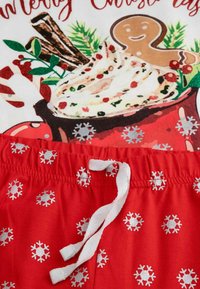 Czerwone szorty piżamowe z białym sznurkiem, zdobione srebrnymi wzorami płatków śniegu. PowAbove nich znajduje się biała koszulka z grafiką w tematyce świątecznej.