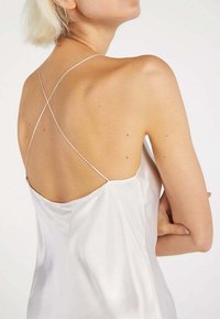 Silk slip dress in white, featuring a low back with crossed straps and a smooth, shiny texture, emphasizing simplicity and elegance.