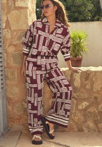 Bordeaux tweedelige outfit met witte gestreepte patronen; oversized shirt met kraag, relaxte wijde broek, en zwarte sandalen.
