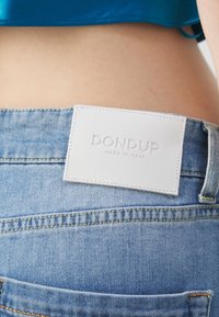 Džíny z denimu s světlým modrým omakem, se zadním koženým štítkem bílého odstínu označeným "DON DUP MADE IN ITALY." Viditelné švy.