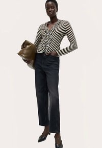 Langærmet, stribet bluse med flæsedetaljer, kombineret med mørke denim-jeans med rette ben og spidse sorte sko, mens hun holder en brun taske.