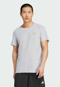 Svetlo šedé tričko s krátkym rukávom s textúrovaným, jemným pruhovaným vzorom a malým šedým logom na hrudi. Mäkka tkanina, okrúhly výstrih.