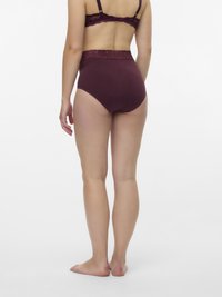 Γυναίκα που στέκεται ξυπόλητη, φορώντας σμαραγδί εσώρουχα και αντίστοιχο σουτιέν με ψηλή μέση, απεικονιζόμενη από πίσω σε λευκό φόντο.