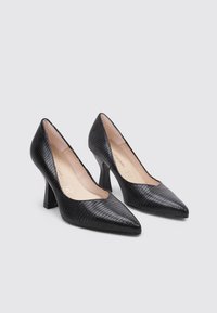 Zapatos de tacón alto negros con un patrón texturizado y en relieve, puntera afilada y tacones de bloque estrechos. El interior cuenta con un forro de color beige claro.