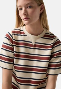 Striped T-shirt in beige with maroon and navy horizontal stripes. V-neckline and short sleeves, made of smooth fabric with a soft texture.