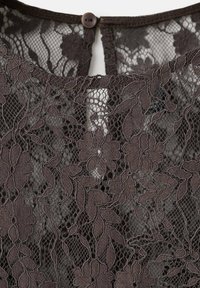 Tissu en dentelle florale noire avec motifs de feuilles, avec une petite fermeture à bouton et boucle sur le bord supérieur.