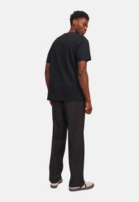 Sort bomulds T-shirt med korte ærmer og rund hals, parret med sorte vide bukser og beige sneakers, set bagfra.