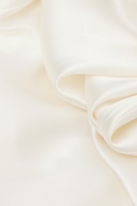 Tela de satén blanco suave y cremosa, doblada con suaves curvas y un sutil brillo, que resalta su textura sedosa.
