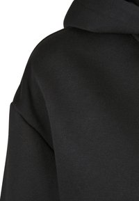 Gros plan sur un tissu de sweat à capuche noir montrant un tricot texturé et une couture d'épaule pliée.