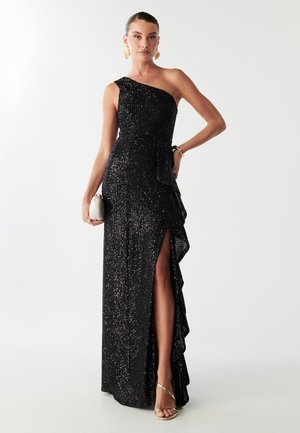 Must musta, ühe õlaga kleit, kaetud hõbedaste säraelementidega, millel on volangiga küljeosa ja kõrge lõhik. Kombineeritud väikese kreemika tingel-tangeliga ja metallik kingadega.