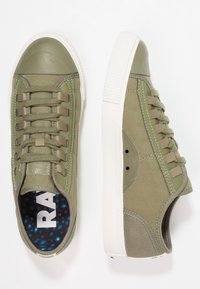 Baskets vert olive avec embout en caoutchouc, dessus en toile, et semelle en caoutchouc blanche. Tissu texturé avec une semelle intérieure multicolore comportant l'inscription "RA."
