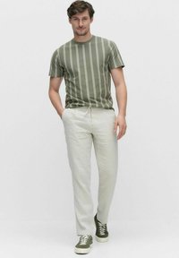 Khaki gestreepte t-shirt, ronde hals, gecombineerd met licht beige broeken, met groene sneakers. Zachte texturen en casual pasvorm.