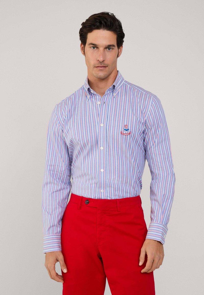 Camisa de botones con rayas verticales azules y rosas, hecha de algodón. Presenta un cuello, mangas largas y un pequeño logo en el pecho.
