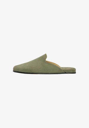 Olivengrøn ruskind slip-on mule med lukket rundet tå og flad sort sål, vist fra siden på en hvid baggrund.