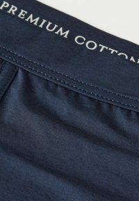 Námořnická modrá prémiová bavlněná látka s hladkou strukturou a jemným prošíváním, s logem vyšitým na horním okraji.