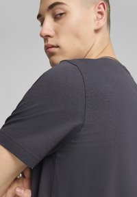 Mørkegrå kortærmet t-shirt med glat tekstur, rund hals og diskret sømdetail på skulderen. Ingen synlige mønstre eller grafik.