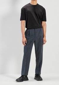 Sort T-shirt med korte ærmer kombineret med mørkegrå plisserede bukser og sorte atletikskøjter, sat mod en neutral baggrund.