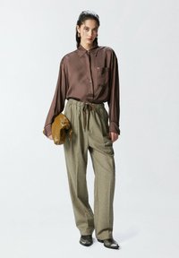 Smeđa satenasta košulja dugih rukava s ovratnikom, uparena s laganim zelenim kariranim hlačama. Drži smeđu torbicu i čizme do gležnja s metalnim vrhom.