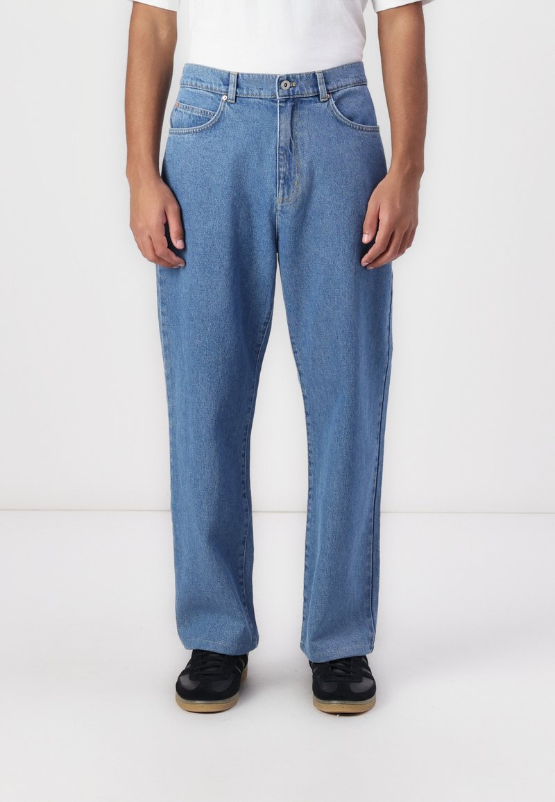 Jean en denim bleu clair avec une coupe droite, cinq poches et un léger effet de délavage à l'avant. Associé à des chaussures noires.