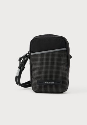 Mustast ruudulise mustriga kandekott, valmistatud tekstuurse kangaga. Varustatud eesalaga ja logoga. Reguleeritav rihm kaasas.