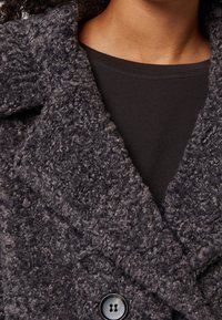 Gray, fuzzy textured coat with a wide collar, featuring a double-breasted design and a prominent black button. Worn over a black top.