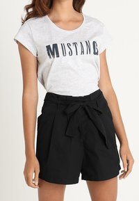 Lys grå T-shirt med "MUSTANG" i mørk tekst, parret med højtaljede sorte shorts med en bundet bælte og flad frontdesign.