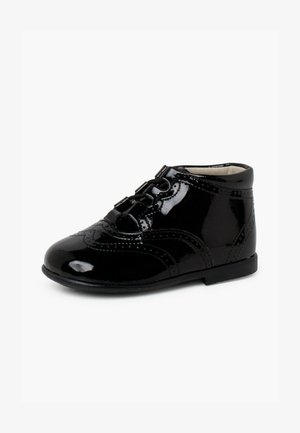 Bottines en cuir verni noir avec un detail brogue, bout rond et lacets noirs. Texture lisse avec une finition légèrement brillante.