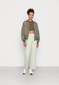 Olive green bomber jacket, cropped black and gold patterned top, mint green wide-leg pants, and white sneakers with neon accents.