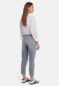 Jean en denim gris avec une coupe fuselée, poignets roulés et deux poches arrière, associé à une chemise blanche à boutons. Baskets noires et blanches.