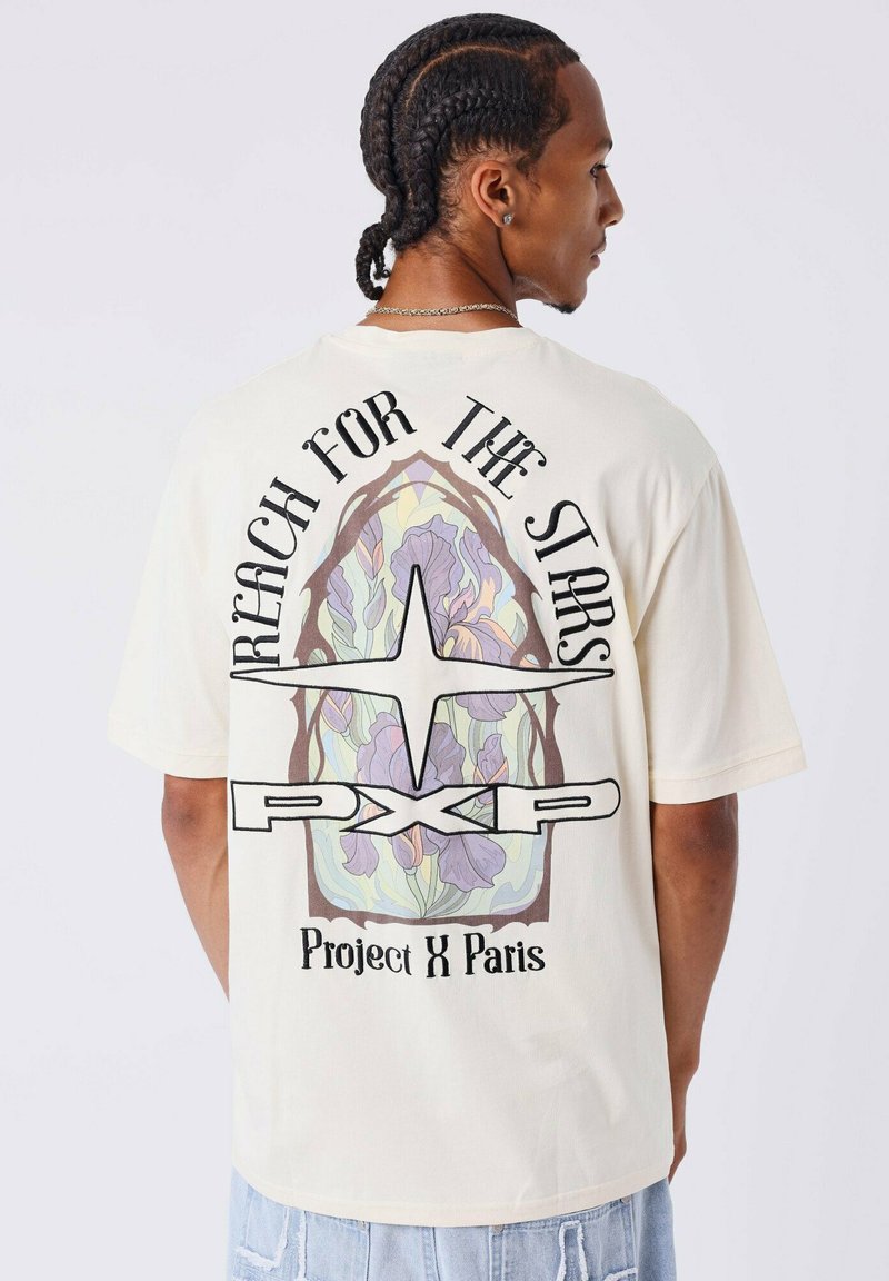 Crème katoenen t-shirt met een grote grafiek met bloemenpatronen in pastelkleuren, zwarte tekst met de woorden "Reach for the Stars" en "Project X Paris."