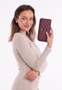 Burgundy faux leather wallet with a quilted design and metal accent. Zipper closure, elongated shape, and side handle for easy carrying.