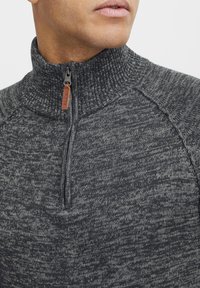 Dark grey zip-up sweater featuring a high collar, textured knit pattern, and a leather accent on the zipper pull.