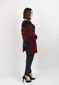 Bordeaux sjal draperet over en sort top, parret med mørke jeans og sorte højhælede sko. Blød tekstur med et åbent, flydende design.
